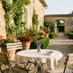 Terrasse de jardin bordelais avec table en fer forgé, chaises en bois et murs en pierre typiques de la Gironde