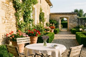 Terrasse de jardin bordelais avec table en fer forgé, chaises en bois et murs en pierre typiques de la Gironde